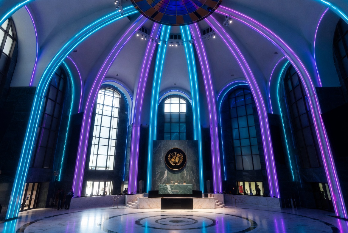 Interior of the United Nations General Assembly Hall with neon cyan and purple lighting, representing multilateral hope and unity